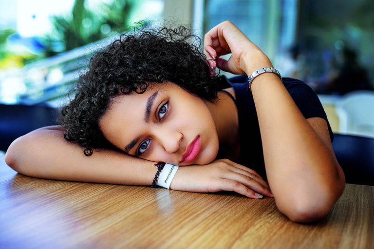A woman with a sad expression, sat at a table, resting her head on her arm on the table